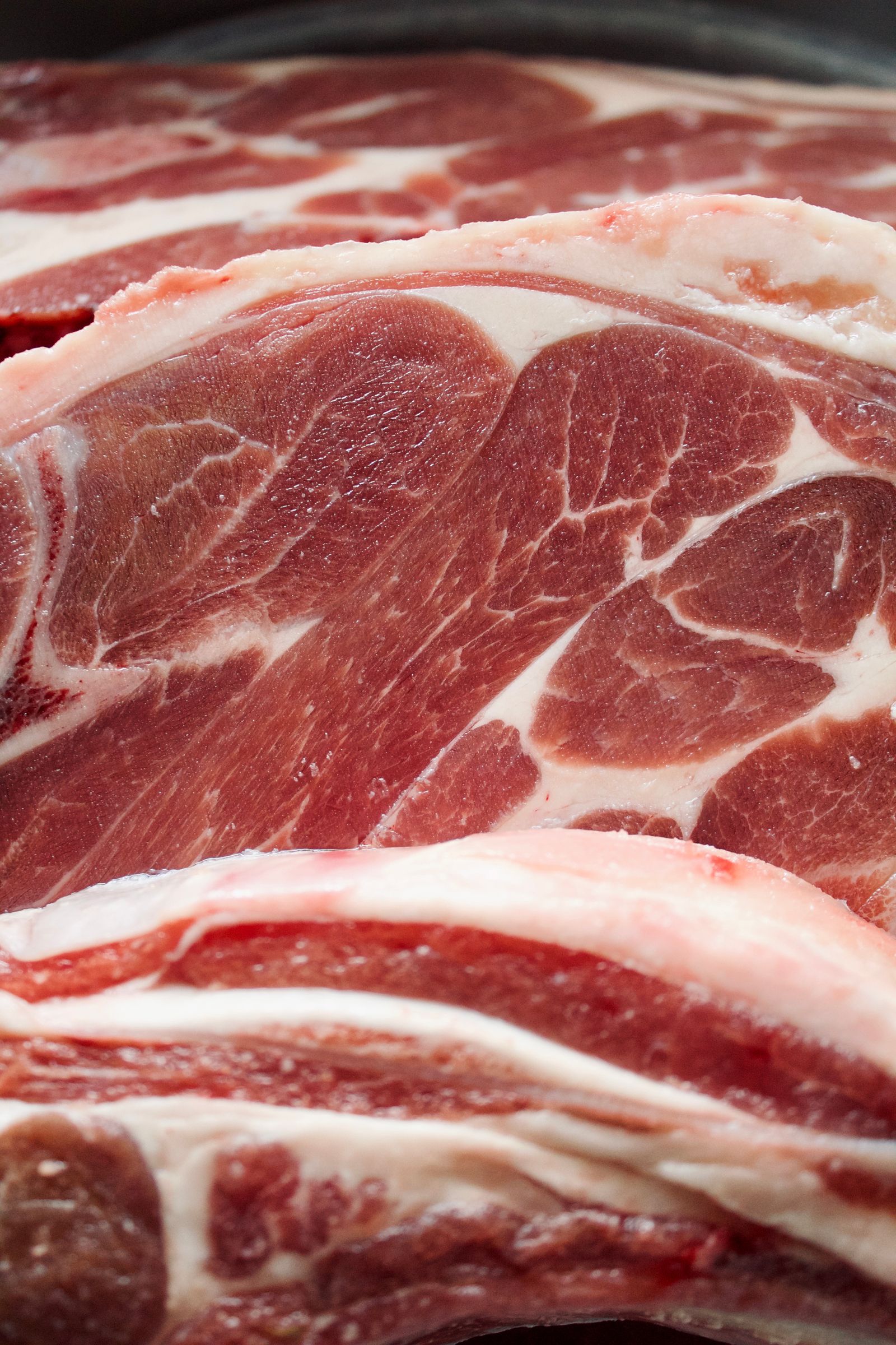 Macro close-up of raw lamb chops showing red meat with white fat marbling and bone edges, filling the frame.